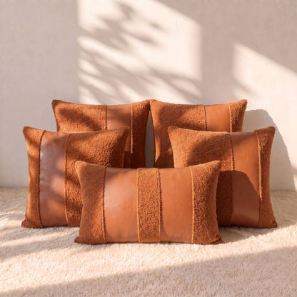 Five warm terracotta pillow covers arranged together, combining curly bouclé fabric with smooth faux leather panels across four square covers and one lumbar cover.
