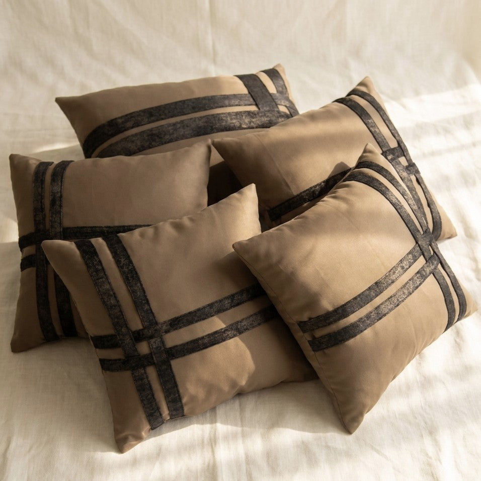 Five warm taupe velvet pillow covers arranged together with intersecting dark printed velvet bands in coordinated geometric designs.
