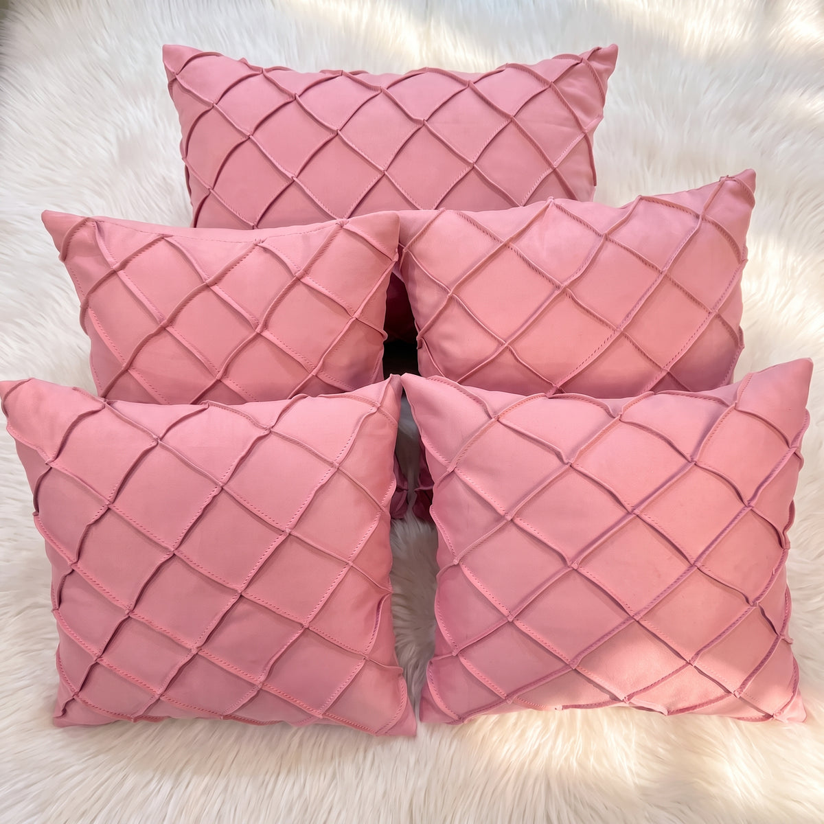 Five dusty rose velvet pillow covers arranged together, featuring raised handwoven geometric diamond lattice detailing.