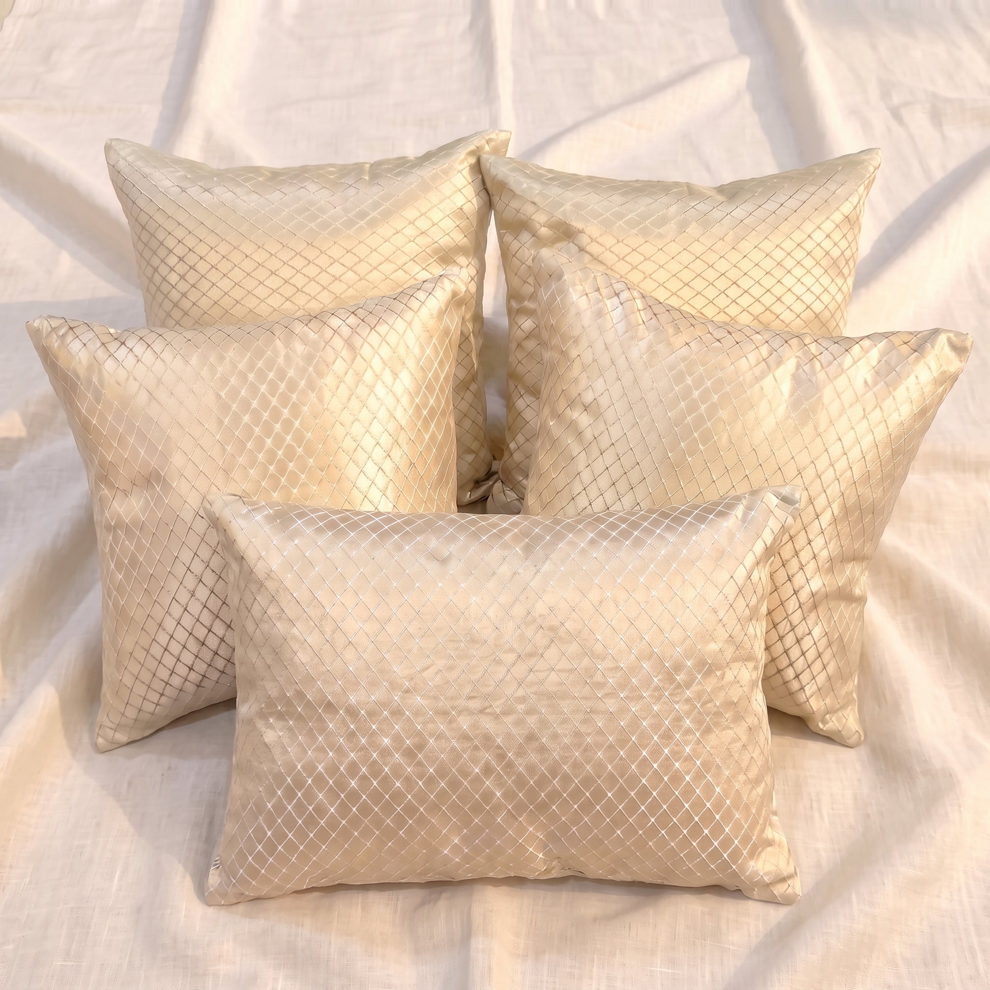 Five champagne-gold jacquard pillow covers arranged together, showing four square covers and one rectangular lumbar cover with a woven geometric lattice pattern.
