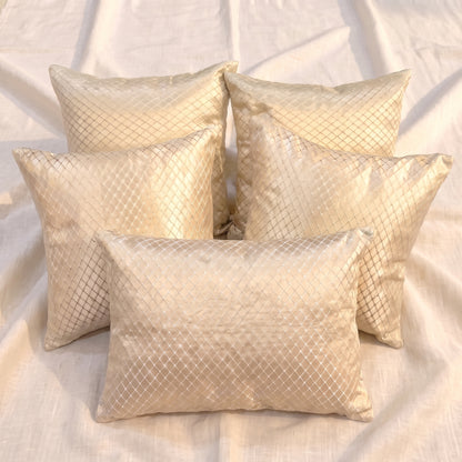 Five champagne-gold jacquard pillow covers arranged together, showing four square covers and one rectangular lumbar cover with a woven geometric lattice pattern.

