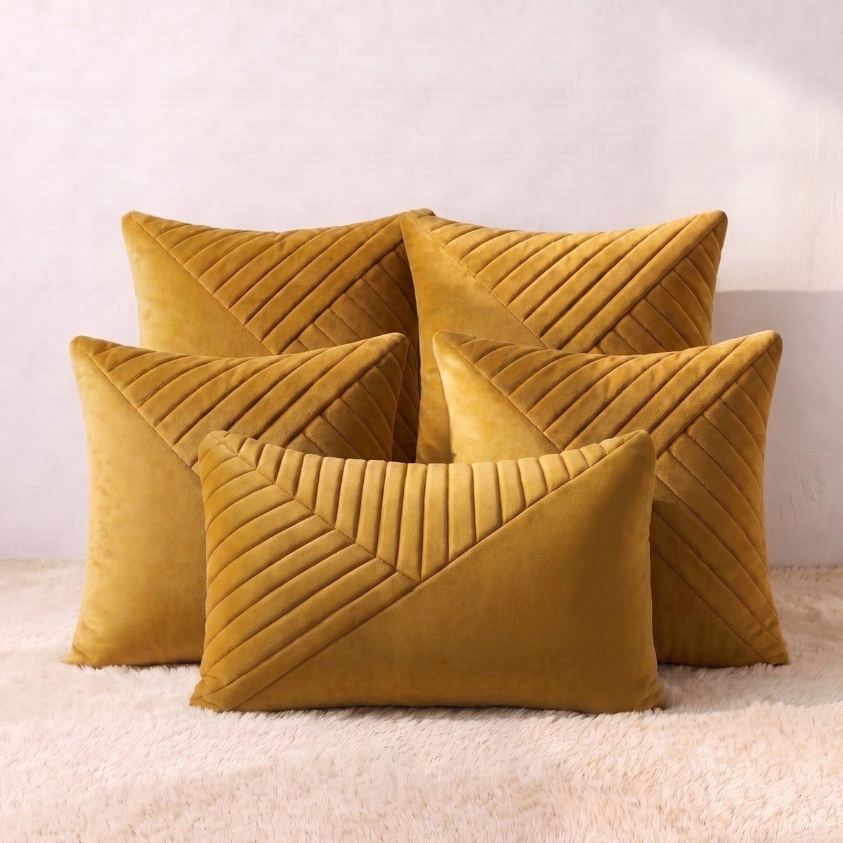 Five mustard-gold velvet pillow covers arranged together, featuring dimensional geometric pleated detailing across the square and lumbar designs.
