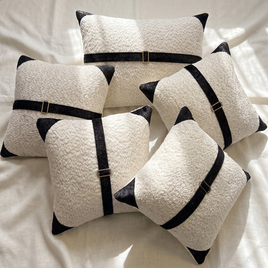 Five white bouclé pillow covers arranged together with contrasting black printed velvet accents and bronze-tone buckle details.