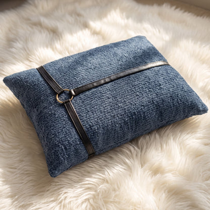 Slate blue bouclé lumbar pillow cover with black faux leather straps meeting at a round gold-tone decorative ring.
