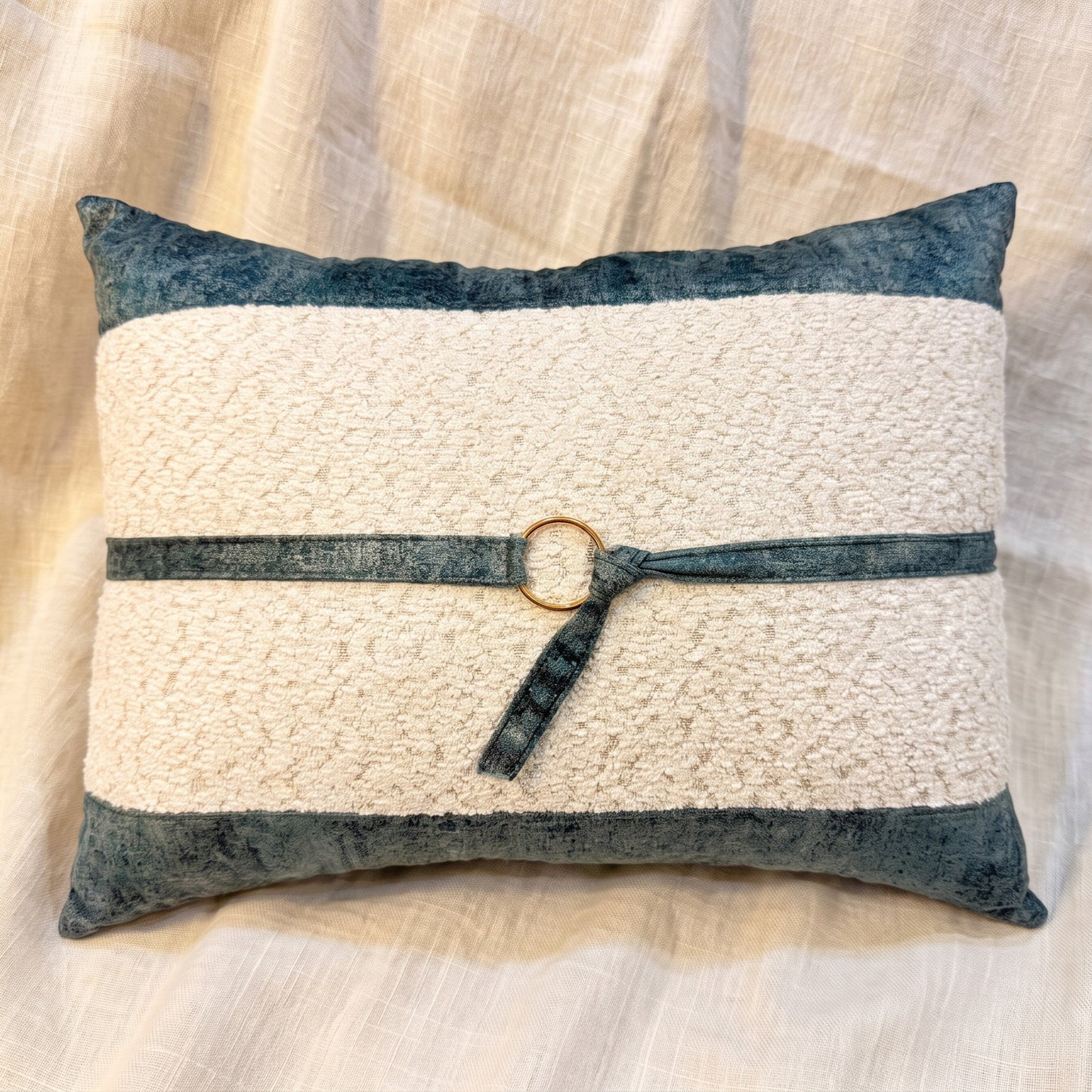 Ivory bouclé rectangular lumbar pillow cover bordered with blue-gray velvet and finished with a matching strap and gold-tone ring.
