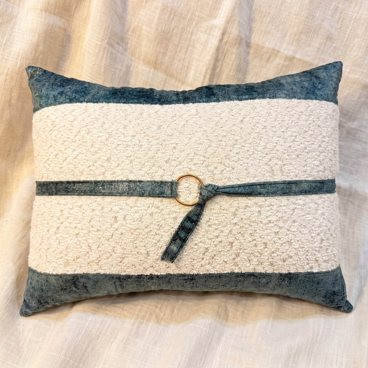Ivory bouclé rectangular lumbar pillow cover bordered with blue-gray velvet and finished with a matching strap and gold-tone ring.
