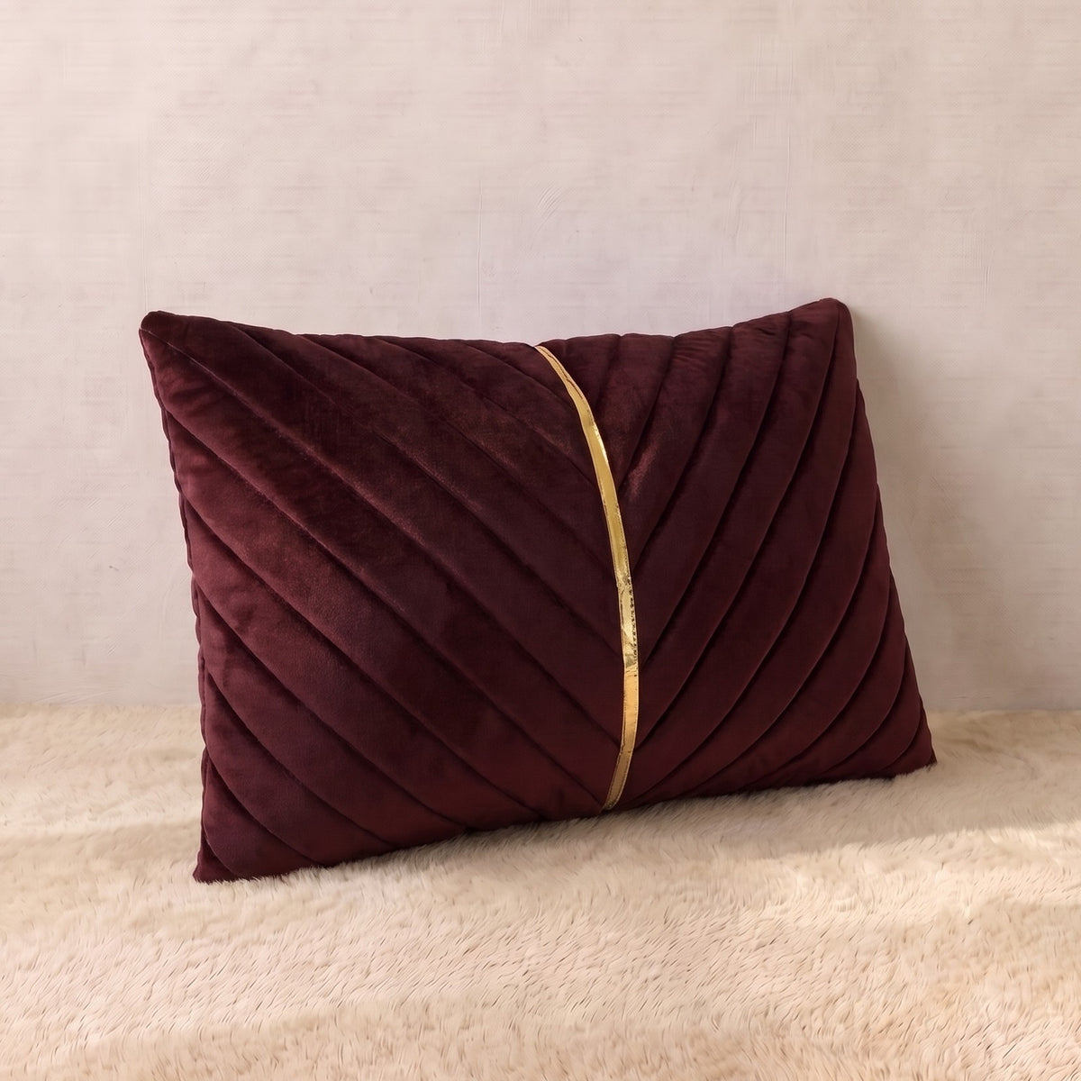 Burgundy velvet lumbar pillow cover with diagonal pleated panels forming a structured V-shaped design and central gold-tone detail.
