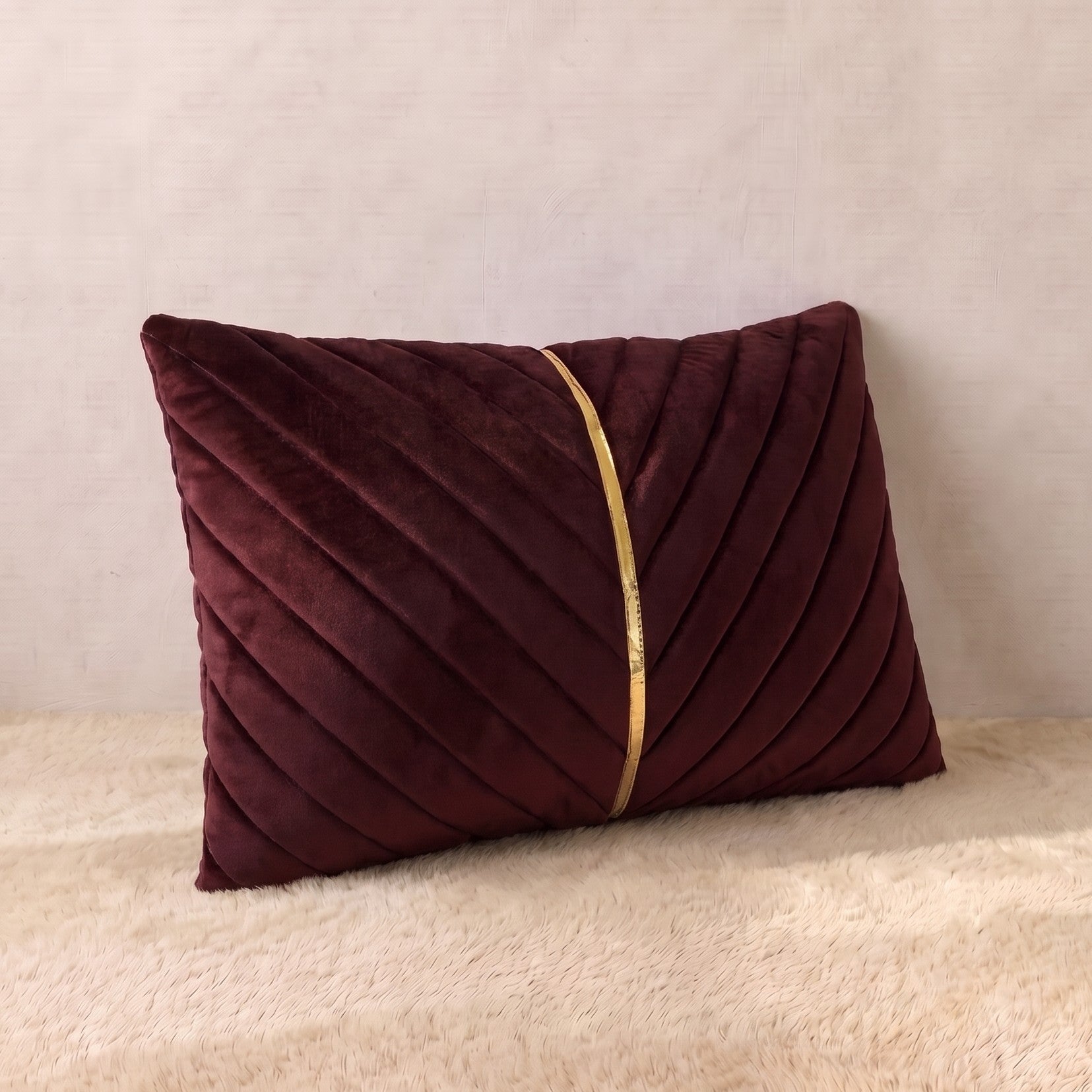 Burgundy velvet lumbar pillow cover with diagonal pleated panels forming a structured V-shaped design and central gold-tone detail.
