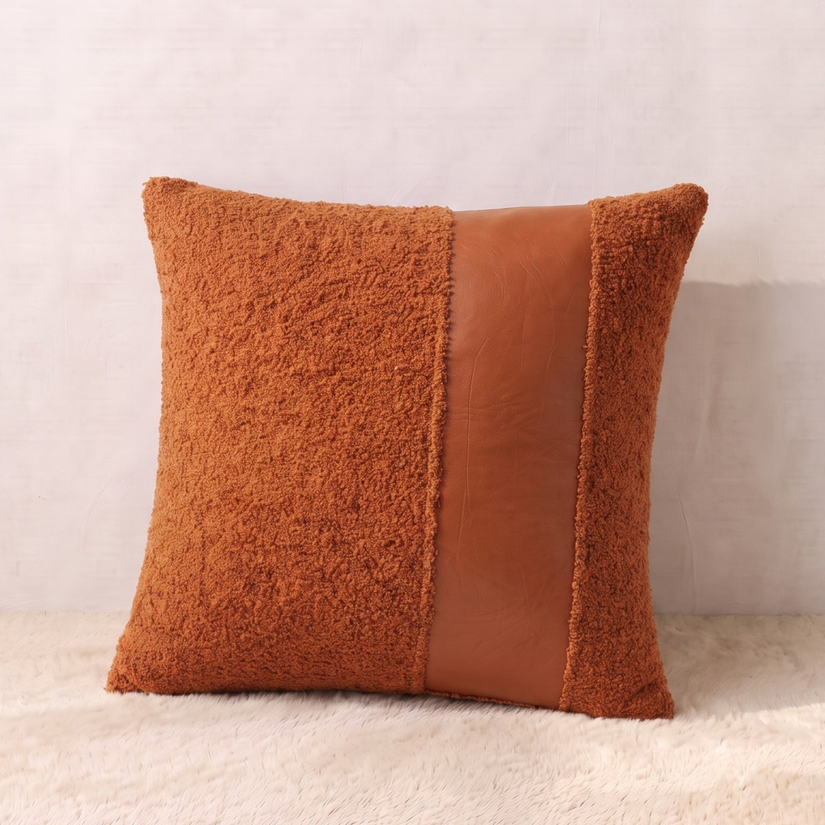 Square terracotta pillow cover combining textured curly bouclé with a smooth faux leather decorative panel.
