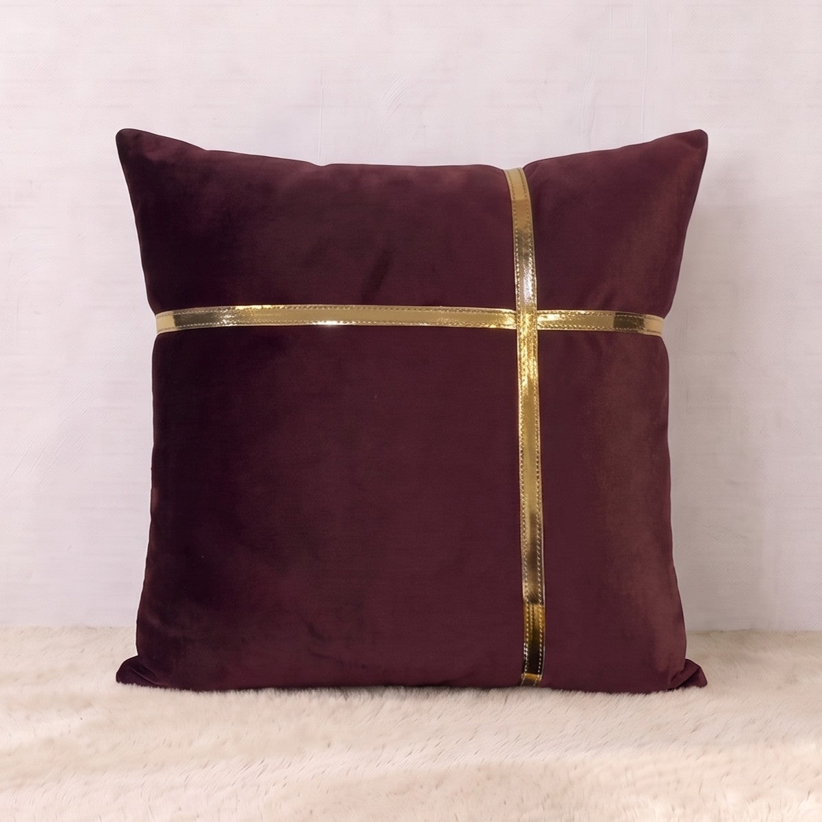 Square burgundy velvet pillow cover with horizontal and vertical reflective gold-tone trim forming a geometric cross design.