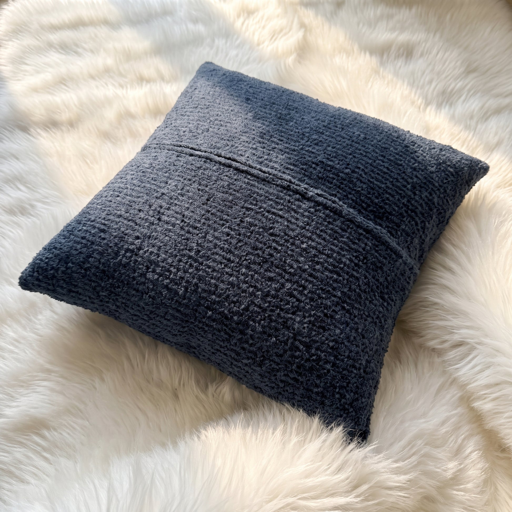 Back view of a slate blue bouclé square pillow cover showing the matching textured fabric and zipper closure.
