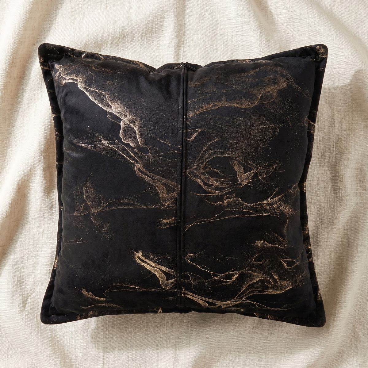 Back of a black and gold printed velvet square pillow cover showing the centered zipper closure.

