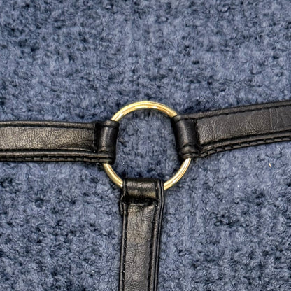 Close-up of black faux leather straps attached around a round gold-tone ring on textured slate blue bouclé fabric.
