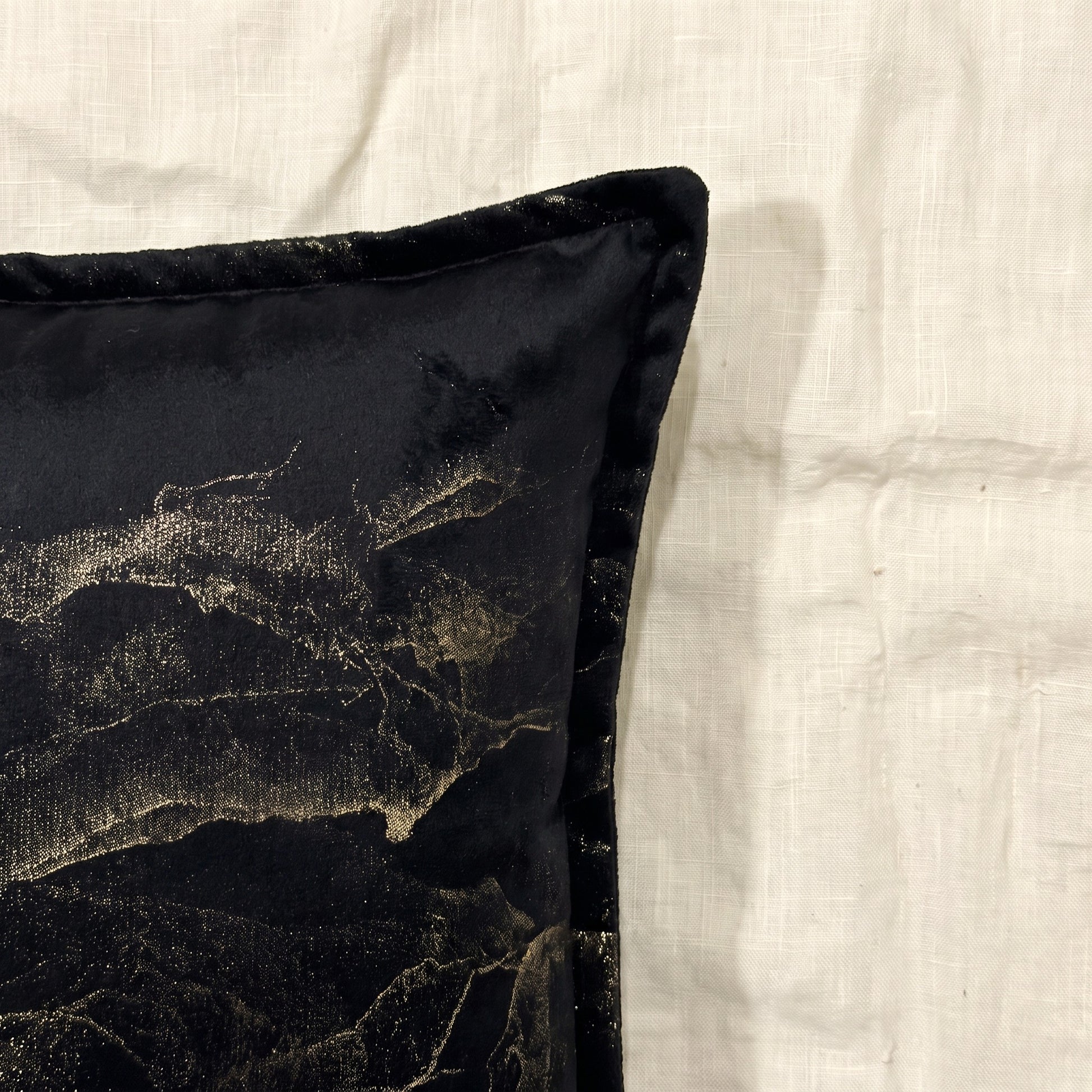 Close-up of black printed velvet showing the flowing gold-toned abstract pattern, soft fabric surface and piped edge.
