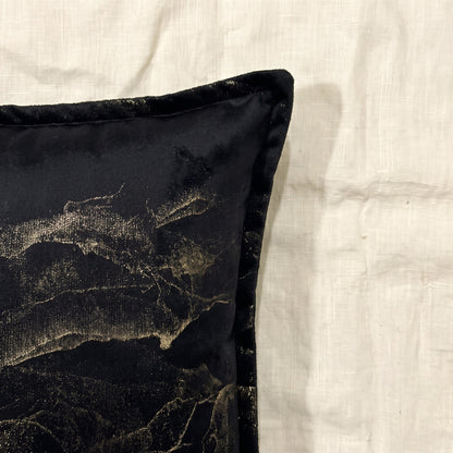 Close-up of black printed velvet showing the flowing gold-toned abstract pattern, soft fabric surface and piped edge.
