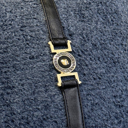 Close-up of gold-tone and black decorative buckle hardware attached to a black faux leather strap over slate blue bouclé.

