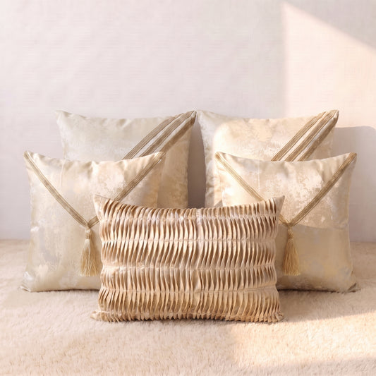 Five champagne-gold jacquard pillow covers arranged together, including tassel designs, decorative gold lace details and one pleated lumbar cover.