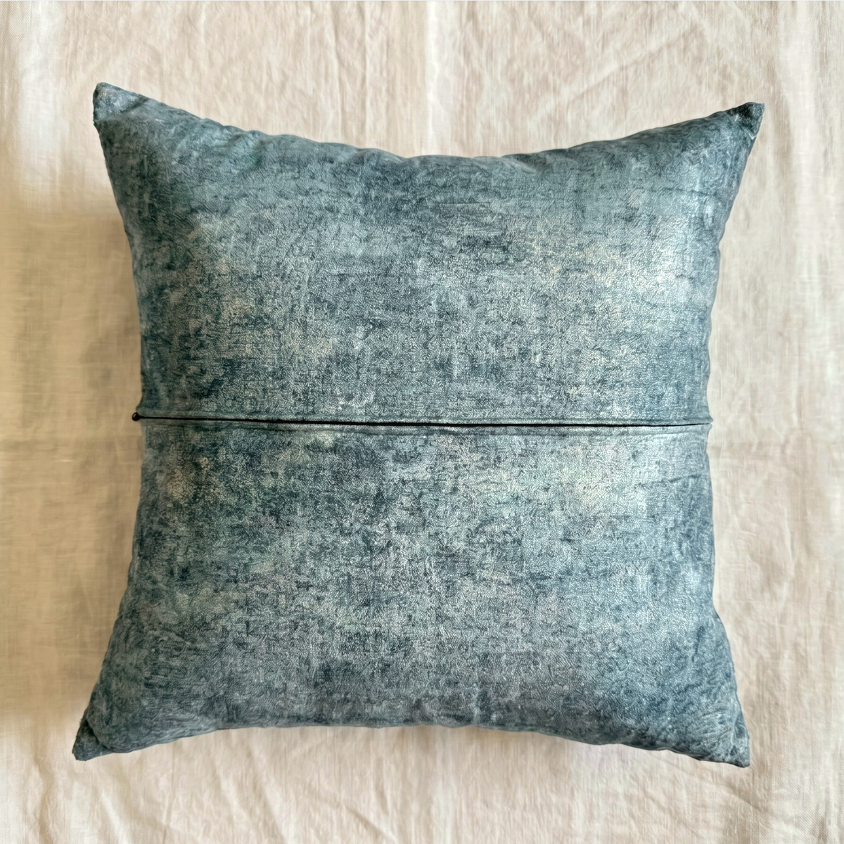 Back of a muted blue-gray velvet square pillow cover showing the matching fabric and horizontal zipper closure.

